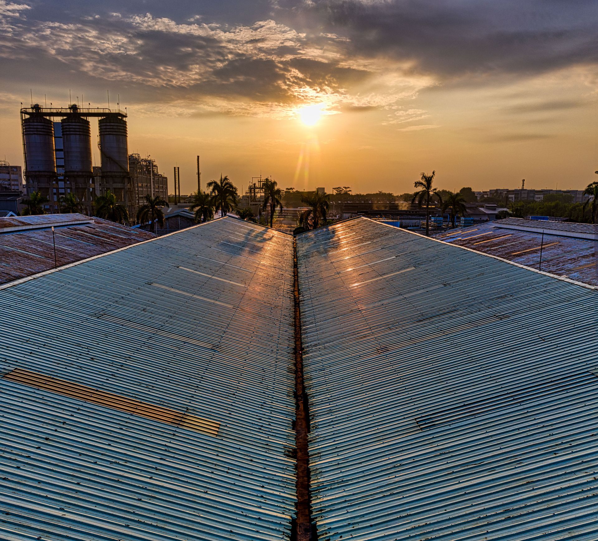 Metal rusty gray roof of construction in industrial area on modern factory in tropical country on sunset against cloudy sky