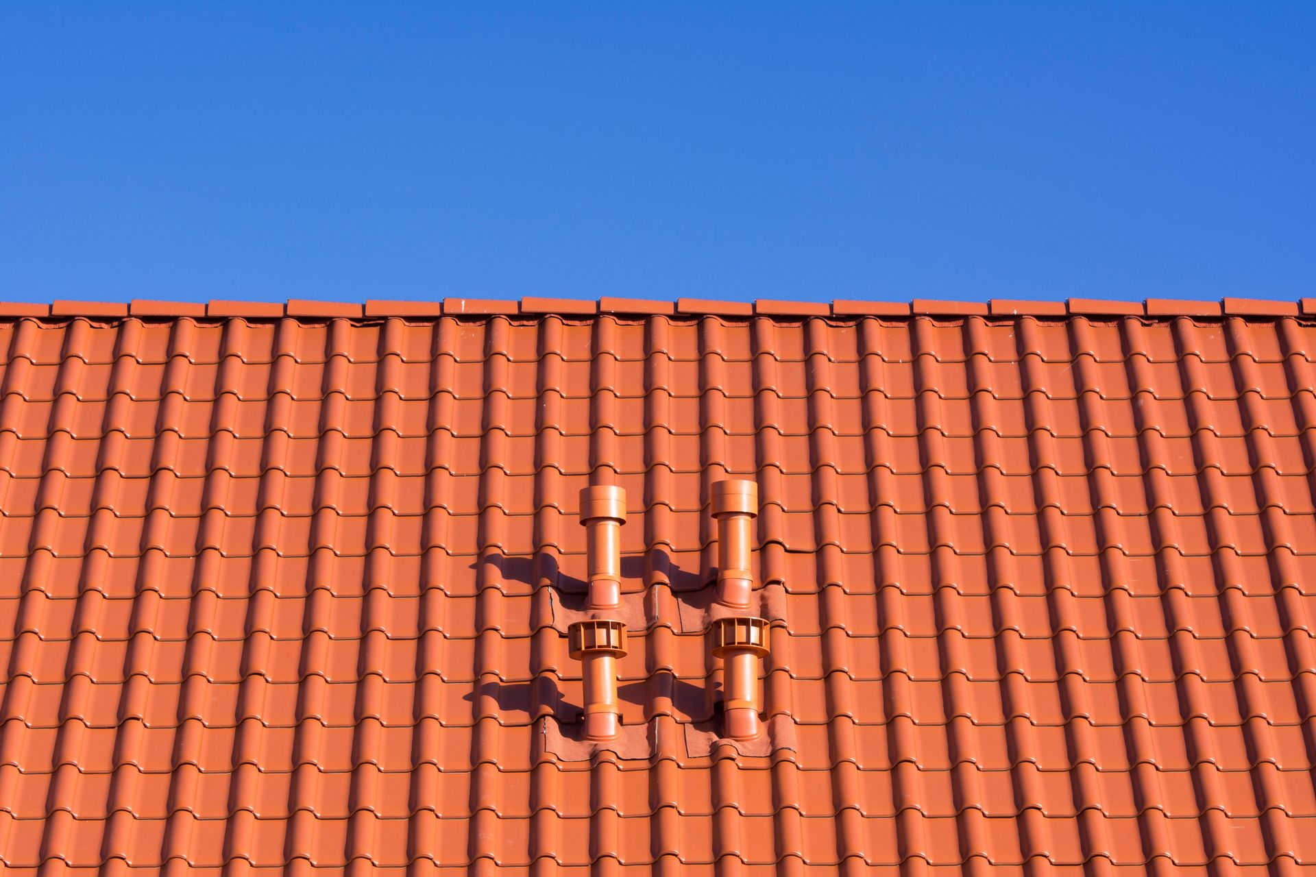 Vivid red clay rooftop with patterns and vents beneath a clear blue sky, ideal for architecture themes.